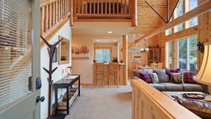 Un vaste espace de vie agrémenté d’un escalier en bois, d’un canapé confortable avec des coussins à carreaux, et d’un coin repas avec une cuisine en arrière-plan.