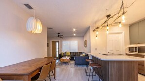 A modern kitchen with a central island, bar stools, and a dining area with a wooden table and chairs. - NEW! Stylish & Cozy Sea Grape near Beach & Flagler (New Smyrna Beach)