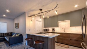 A modern kitchen with a central island, dark wooden cabinets, a stainless steel refrigerator, and a unique light fixture. - NEW! Stylish & Cozy Sea Grape near Beach & Flagler (New Smyrna Beach)