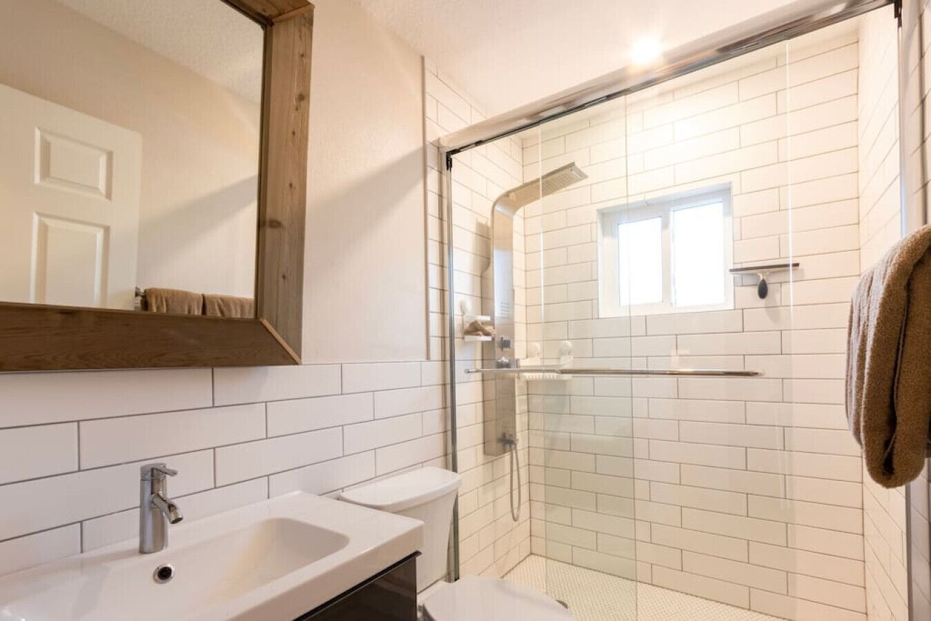 Une salle de bain moderne avec une douche en verre, des murs recouverts de carreaux blancs, un plafond en bois et un grand miroir.