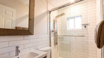Une salle de bain moderne avec une douche en verre, des murs recouverts de carreaux blancs, un plafond en bois et un grand miroir.