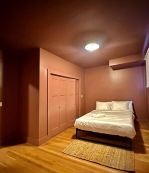 Une chambre à coucher avec un lit, un plancher en bois, un placard et un luminaire au plafond.