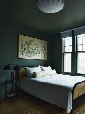 A bedroom with a bed, a bedside table, a lamp, and a window. - Elm Grove Co.Housenhv (Downtown New Haven)