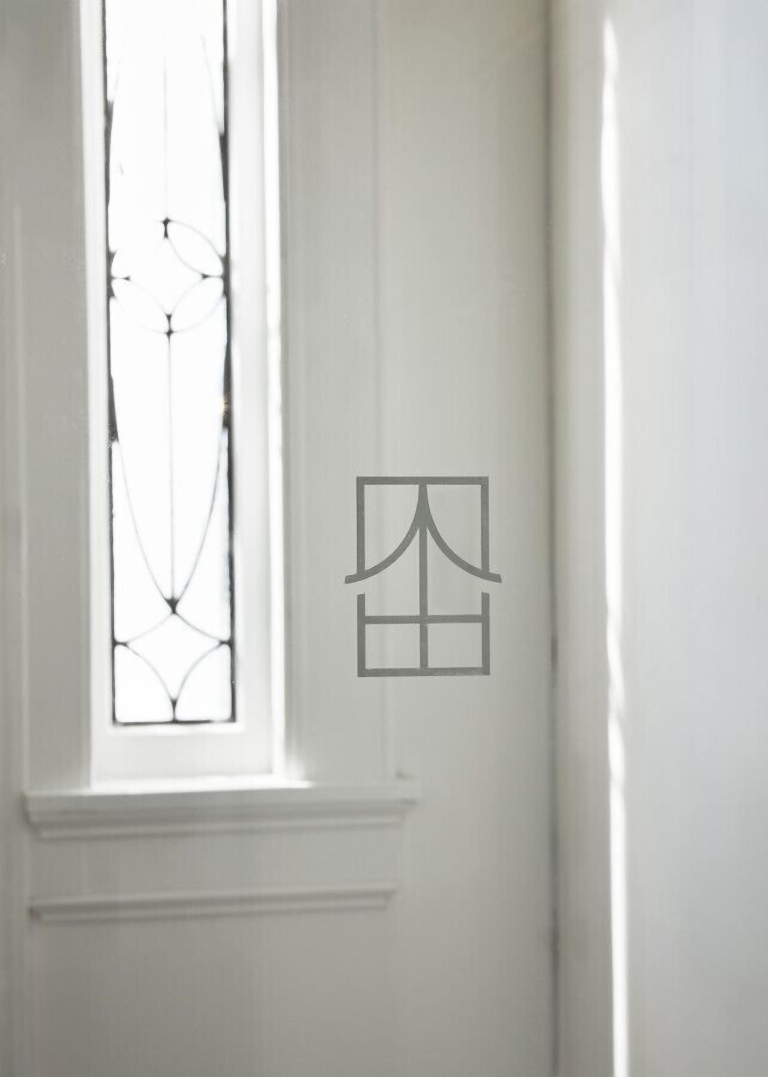 Une porte blanche ornée d’une fenêtre avec un vitrail aux motifs géométriques.