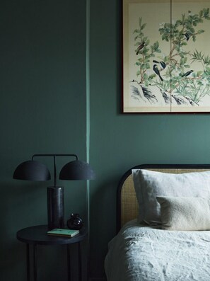 A room with a bed, a nightstand with a lamp, and a painting on the wall. - Elm Grove Co.Housenhv (Downtown New Haven)