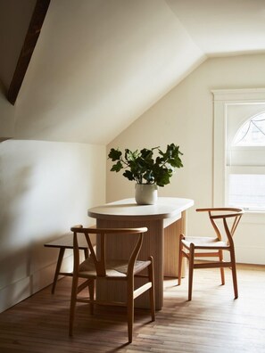 A small, cozy room with a sloped ceiling, a round wooden table, two wooden chairs, and a potted plant.