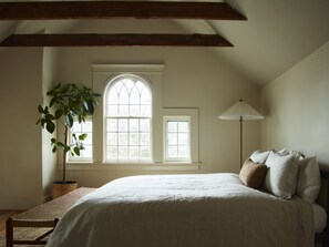 A bedroom with a large bed, a potted plant, two windows, and a floor lamp.