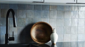 Eine Küche mit grauen Schränken, einem schwarzen Wasserhahn, einer Holzschüssel und einer weißen Vase auf der Arbeitsfläche.