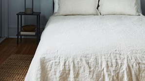 Ein Schlafzimmer mit einem Bett, zwei gerahmten Kunstwerken an der Wand, einem Nachttisch mit einer Lampe und einem kleinen Hocker.