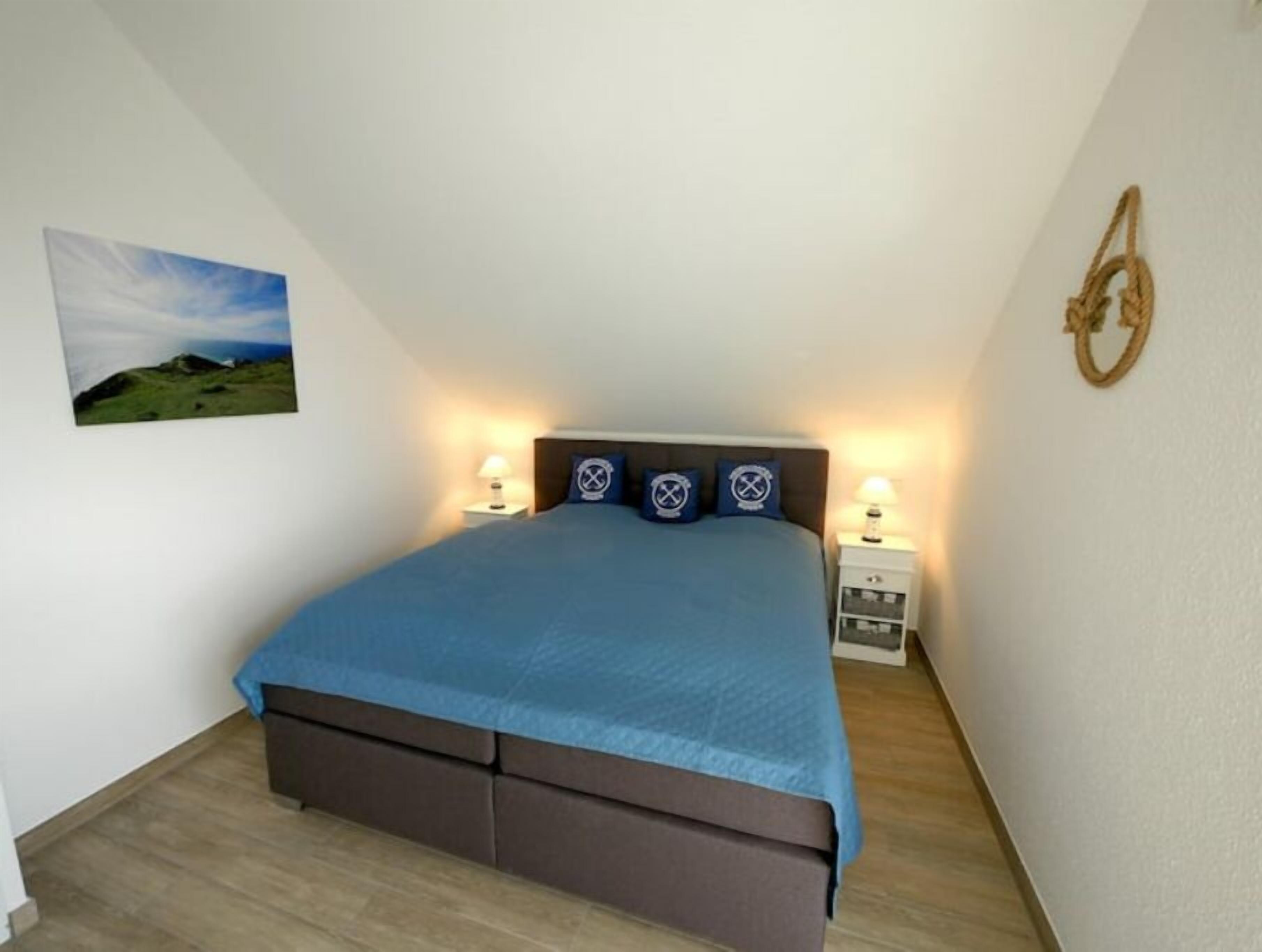Ein Schlafzimmer mit einem Bett, zwei Nachttischen, einer Wandlampe und einem Landschaftsbild.