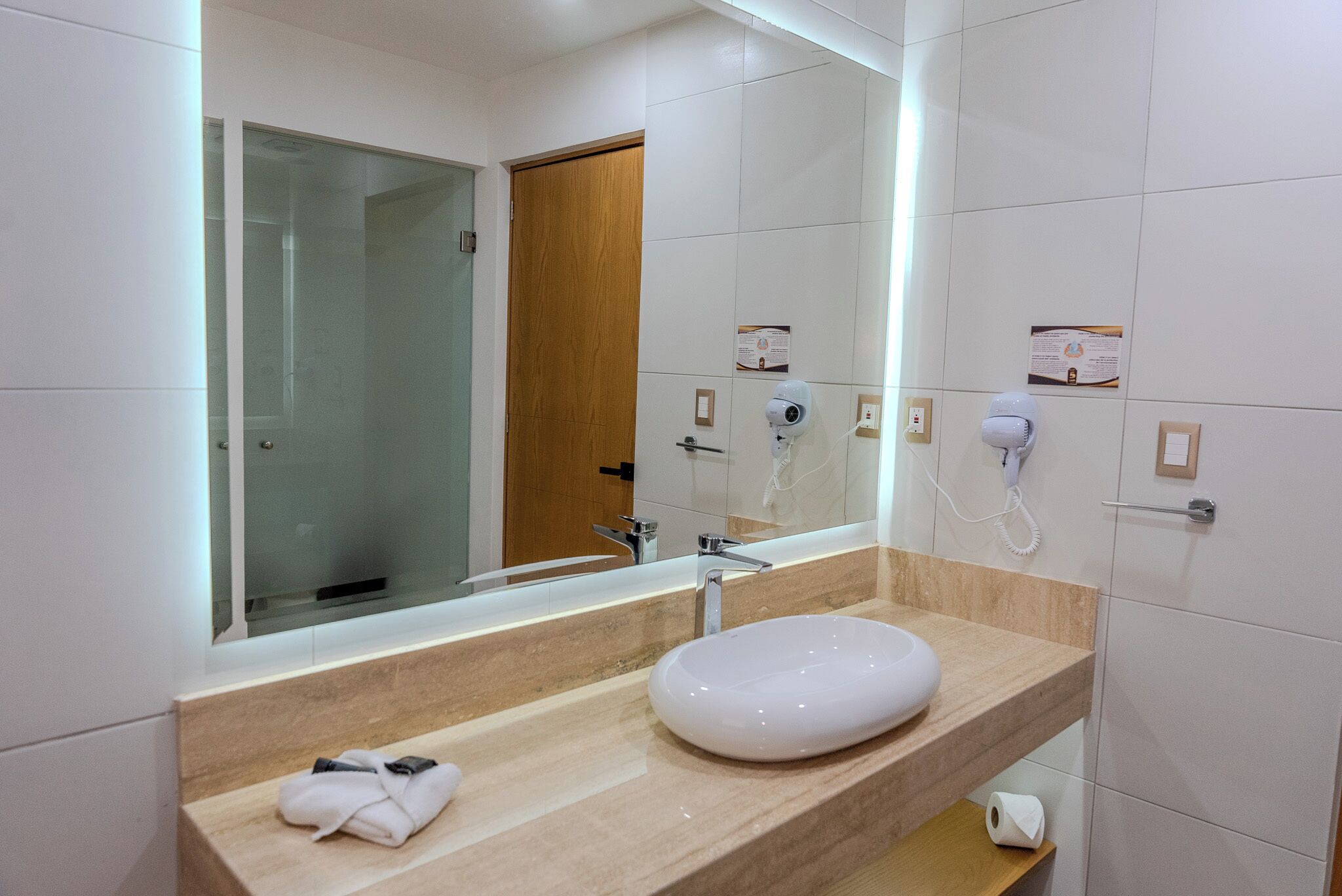 Un baño moderno con un espejo grande, un lavabo blanco, una toalla y un secador de pelo.