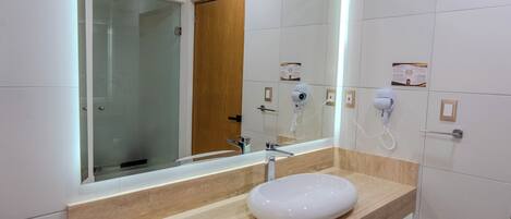 Un baño moderno con un espejo grande, un lavabo blanco, una toalla y un secador de pelo.
