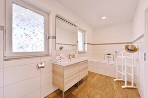 A modern bathroom with a large window, a vanity with a mirror, a bathtub, and a towel rack.