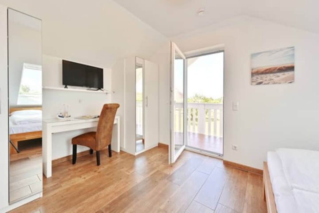 A room with a bed, a desk, a chair, a television, and a sliding glass door leading to an outdoor area.