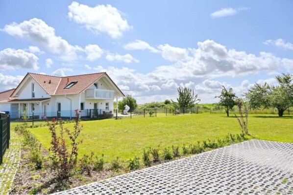 A two-story house with a red-tiled roof, a large front lawn, and a clear sky.