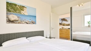 A bedroom with a bed, a nightstand, a dresser, and a painting of a coastal scene. - Villa Meereszeit (Trent)