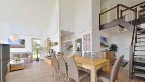 A spacious living area with a wooden dining table, comfortable seating, a staircase, and a view of the outdoors. - Villa Meereszeit (Trent)