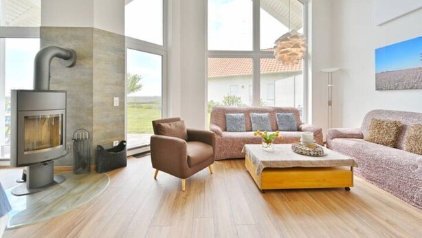 A modern living room with a fireplace, large windows, a sofa, and a coffee table. - Villa Meereszeit (Trent)