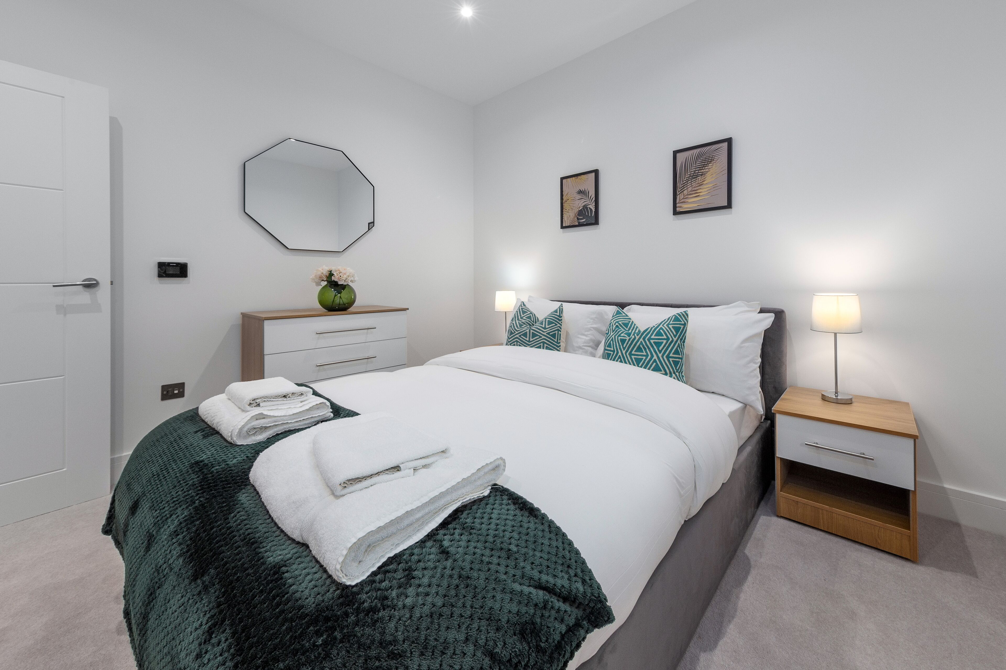 Quarto bem organizado com cama, mesas de cabeceira, espelho e quadros nas paredes.