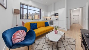 A modern living room with a sofa, chairs, a coffee table, and a view of the kitchen. - SERCASA - Appletree Court - Kingston (Kingston Upon Thames)