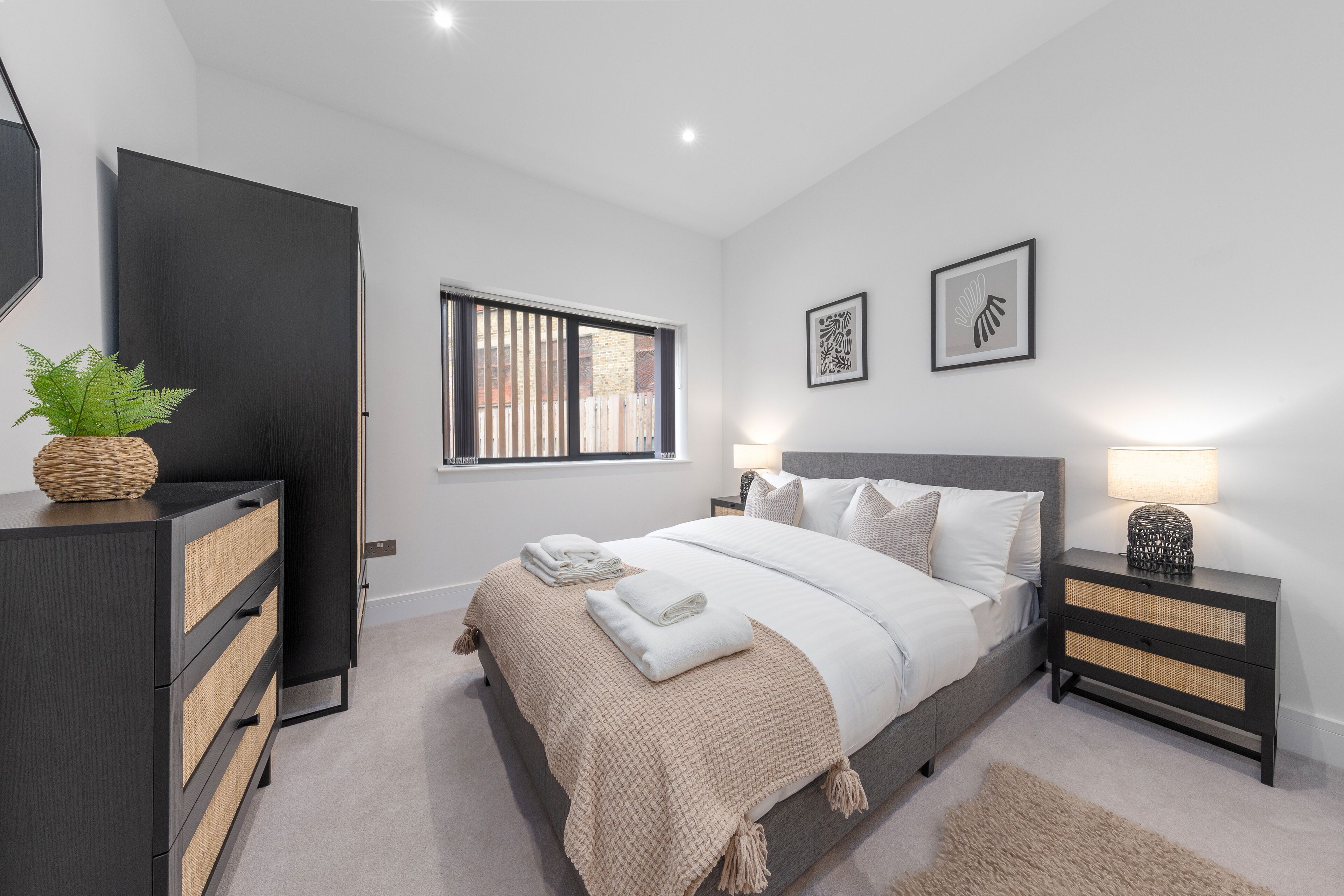 A modern bedroom with a bed, bedside tables, a dresser, and a window.