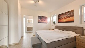 A modern bedroom with a large bed, a bedside table, a wardrobe, and two paintings on the wall.