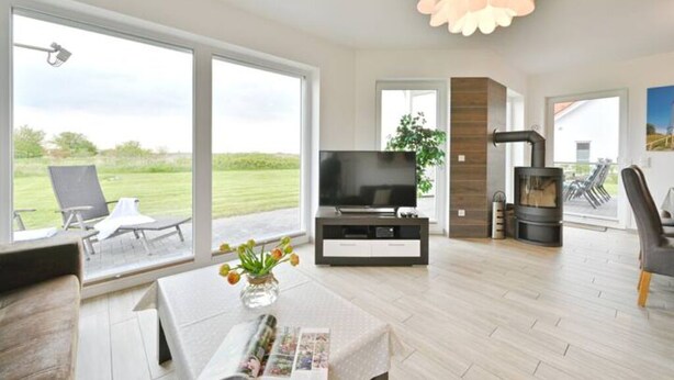 A modern living room with a TV, fireplace, and large windows overlooking a garden.