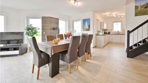 A modern kitchen with a central island, a dining area with a wooden table and chairs, and a staircase leading to an upper level.