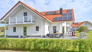A modern house with a red-tiled roof, solar panels, a balcony, and a patio with outdoor furniture.