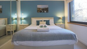 A neatly made bed with a blue and white patterned bedspread, two bedside lamps, a nightstand, a mirror, and a window with a view of trees. - Fabulous 3 bedroom property in city centre location. Sleeps 5. (Edinburgh)