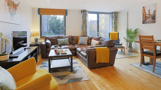 A modern living room with a brown leather sofa, a yellow armchair, a coffee table, and a dining area with a wooden table and chairs. - Fabulous 3 bedroom property in city centre location. Sleeps 5. (Edinburgh)