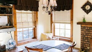 A cozy room with a wooden ceiling, a chandelier, a fireplace, a round table with chairs, and a television on a shelf. - Sagewood Cabin @ Whispering Oaks, 20 miles from Moab! (Moab)