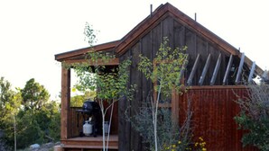 A rustic wooden cabin with a porch, surrounded by greenery and wildflowers. - Sagewood Cabin @ Whispering Oaks, 20 miles from Moab! (Moab)
