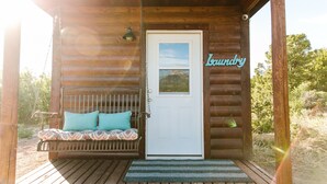 A wooden cabin with a white door, a bench with cushions, and a sign reading "Laundry". - Wildflower Cabin @ Whispering Oaks, 20 miles from Moab! (Moab)