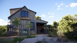 A rustic wooden house with a porch, surrounded by natural vegetation. - Wildflower Cabin @ Whispering Oaks, 20 miles from Moab! (Moab)