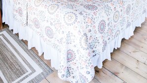 A bedroom with a large bed, floral bedding, a sunflowers painting, and a wooden floor. - Wildflower Cabin @ Whispering Oaks, 20 miles from Moab! (Moab)