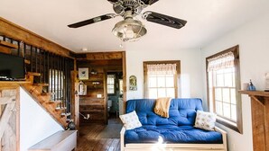 A cozy room with a blue sofa, wooden staircase, and a ceiling fan. - Grey Dawn Cabin @ Whispering Oaks, 20 miles from Moab! (Moab)