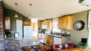 A kitchen with wooden cabinets, a central island with stools, a microwave, and a clock on the wall. - Daybreak Cabin @ Whispering Oaks, 20 miles from Moab! (Moab)