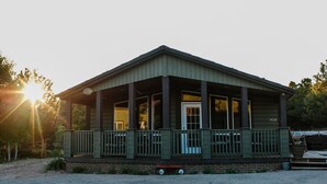 A wooden building with a porch, large windows, and a door. - Daybreak Cabin @ Whispering Oaks, 20 miles from Moab! (Moab)