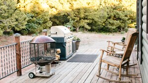 A wooden deck with a grill, a barbecue, and a rocking chair. - Daybreak Cabin @ Whispering Oaks, 20 miles from Moab! (Moab)