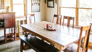 A dining room with a large wooden table, six chairs, a bench, and a hanging light fixture. - Jaydee's Run Cabin @ Whispering Oaks, 20 miles from Moab! (Moab)