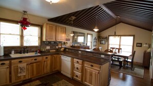 A spacious kitchen with wooden cabinets, a central island, and a dining area with a table and chairs. - Jaydee's Run Cabin @ Whispering Oaks, 20 miles from Moab! (Moab)