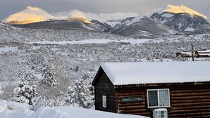 A wooden cabin named "Sandi's Corner" with a snow-covered roof, surrounded by a snowy landscape and mountains in the background. - Jaydee's Run Cabin @ Whispering Oaks, 20 miles from Moab! (Moab)