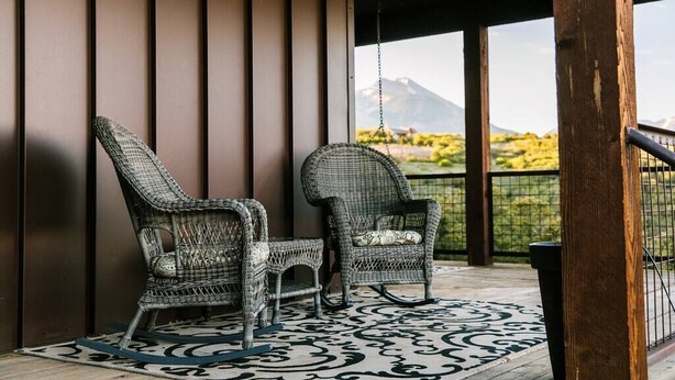 A covered outdoor seating area with wicker chairs and a patterned rug, overlooking a mountainous landscape. - Lonebranch Cabin @ Whispering Oaks, 20 miles from Moab! (Moab)