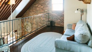 A loft-style room with exposed wooden beams, a brick wall, a large window, a mounted deer head, a grey sofa, and a round rug. - Lonebranch Cabin @ Whispering Oaks, 20 miles from Moab! (Moab)