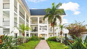 A multi-story hotel with a central entrance, palm trees, and a pathway leading to the entrance. - Simply step across the street from this condo to reach Florida's premier beach! (Siesta Key)