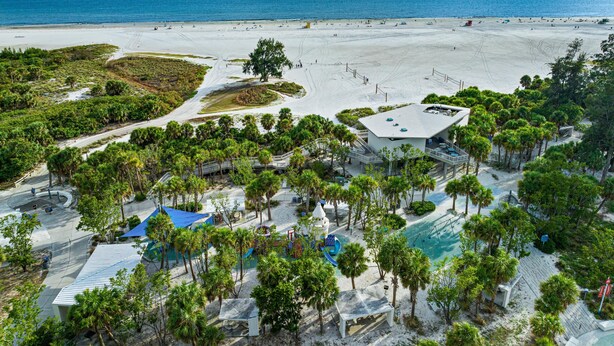 A beach resort with a pool area, palm trees, and a view of the ocean. - Simply step across the street from this condo to reach Florida's premier beach! (Siesta Key)