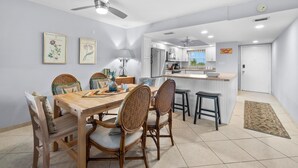 A modern kitchen with white cabinets, a central island, and a dining area with wooden chairs and a table. - Simply step across the street from this condo to reach Florida's premier beach! (Siesta Key)