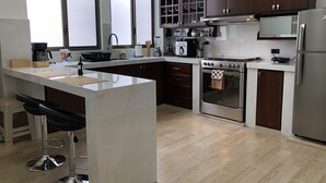 Una cocina moderna con una isla central, armarios de madera oscura, electrodomésticos de acero inoxidable y un amplio ventanal que proporciona luz natural.