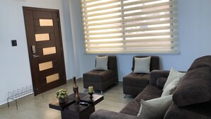 Una sala de estar moderna con un conjunto de sofá marrón, una mesa de centro con objetos decorativos y un ventanal con persianas.